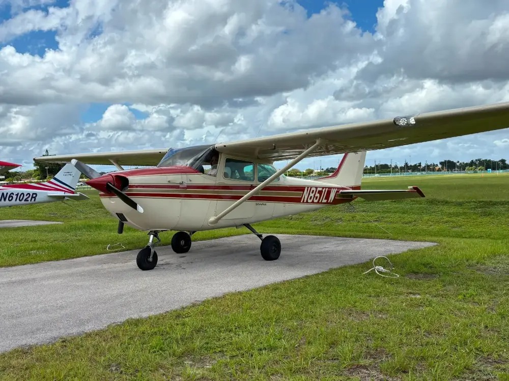 Single-engine airplane parked on a concrete pad by grass